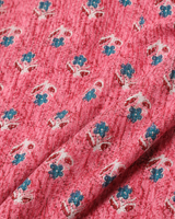A close-up of a pink textured fabric with a repeating block-print pattern of small blue flowers and white leafy stems.