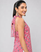 A woman modeling a sleeveless pink floral printed top with a tie-neck detail, shown from a side-back angle against a light gray studio background.